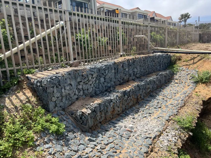Stone-filled gabion cages in front of the rebuilt retaining wall below the fence in Umhlanga.