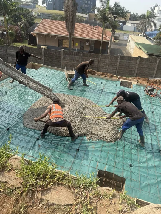 Crew placing concrete over reinforcing mesh for a garage floor slab.