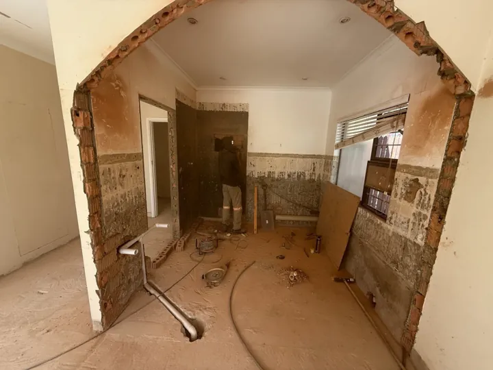 Stripped interior space with an opened wall and exposed masonry before renovation.