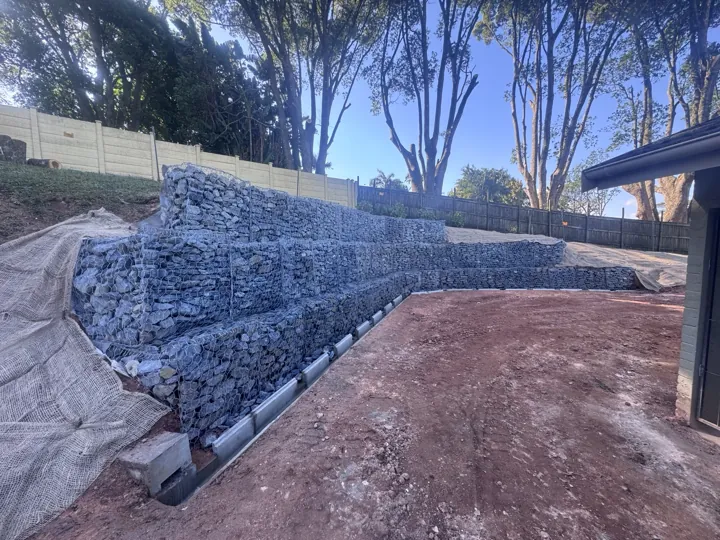 Completed stone-filled gabion retaining wall in Hillcrest, with bare soil and erosion covering around the wall.