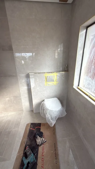 Tiled bathroom walls around a wall-hung toilet and concealed-cistern access opening.