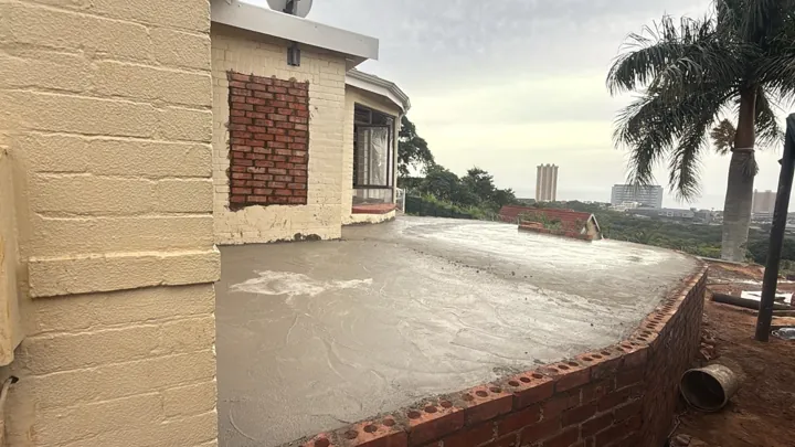 Concrete balcony slab beside the house, with supporting brickwork below.