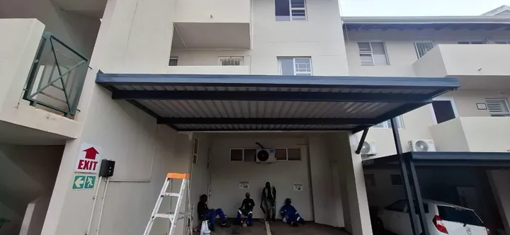 IBR awning on a steel frame above an exterior entrance, with a ladder on site.