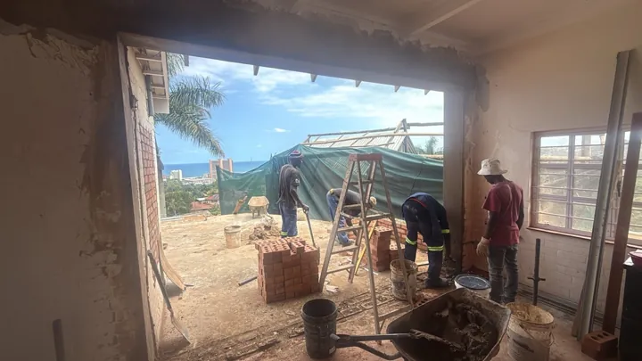 Large broken-out wall opening with overhead steelwork and construction underway.