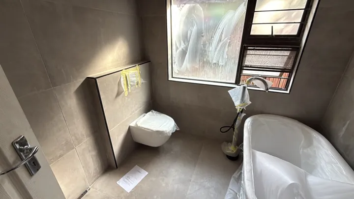 Bathroom with wall-hung toilet, bath and tiled surfaces during fitting work.