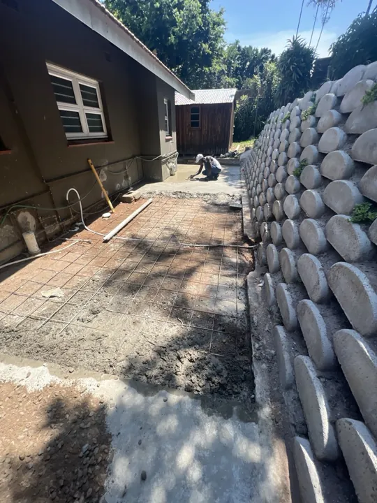 Fresh concrete beside a tall retaining wall adjacent to a house.