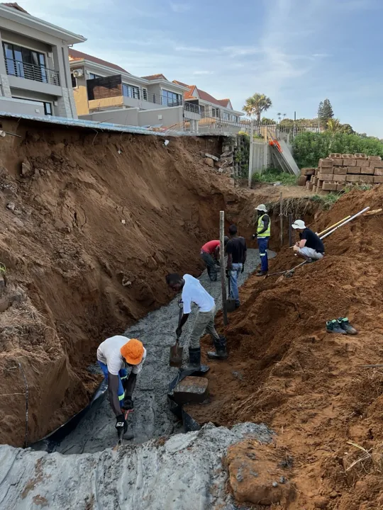 Crew placing concrete in a foundation trench below a coastal property.