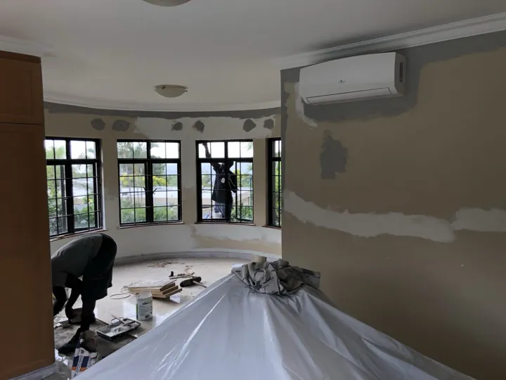 Bedroom walls with patch repairs and protected bed during surface preparation.