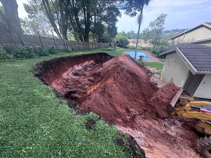 Excavated red-earth embankment beside a lawn before gabion assembly.