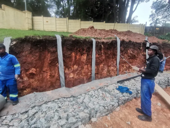 Stone-filled gabion wall and crew beside the excavated embankment.